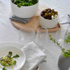 Elegant white dinnerware with a neutral cloth, accented by green salad and wooden serving tray, showcasing a modern dining setup.