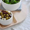 White circular bowls with olives and feta on a light wood tray; green salad in a white bowl on a patterned napkin.