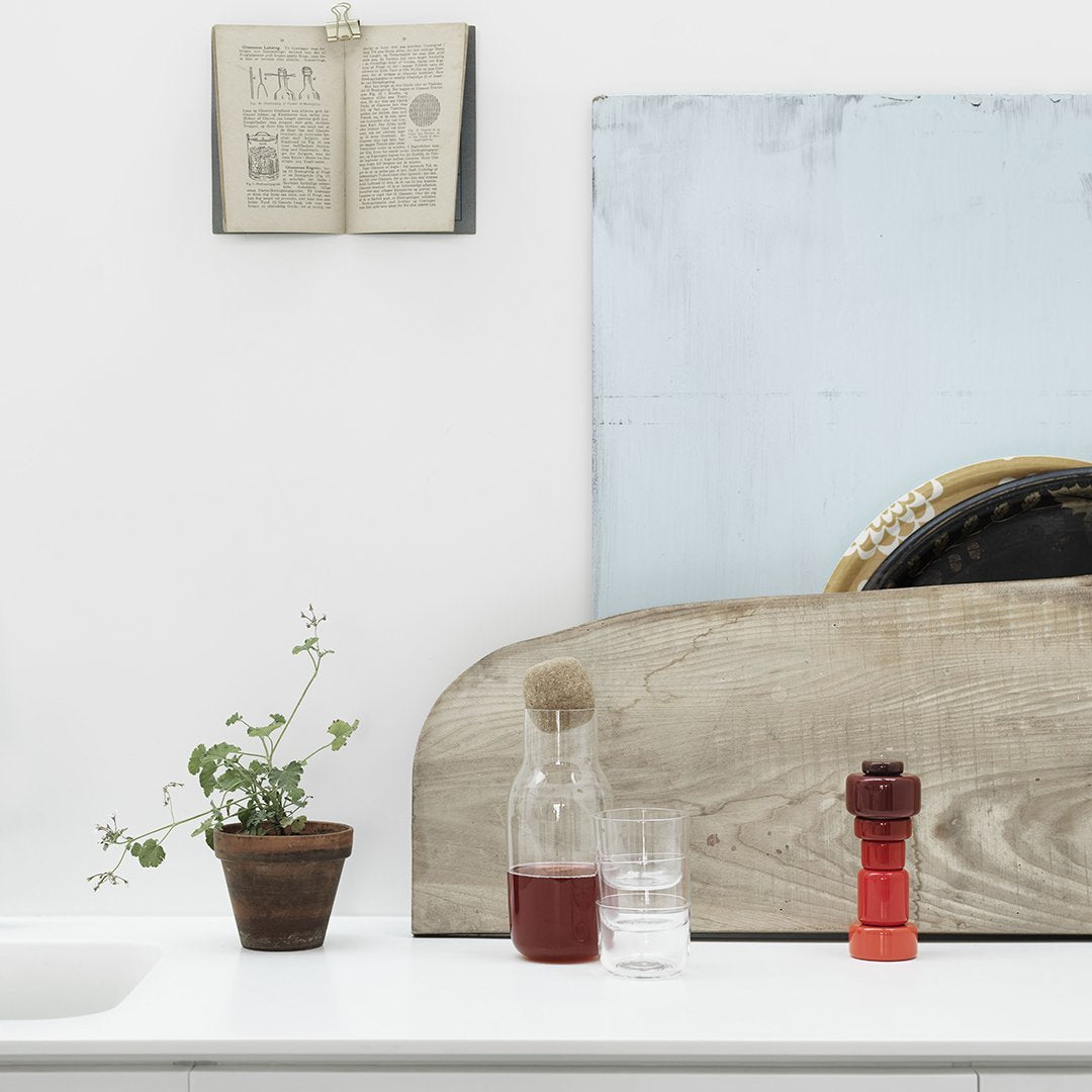 Colorful glassware on a neutral background, featuring red, clear, and earthy tones with green plant accents.