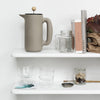 Gray ceramic pitcher with wooden knob, clear glass jars, and minimalist design on white shelves. Simple and modern style.