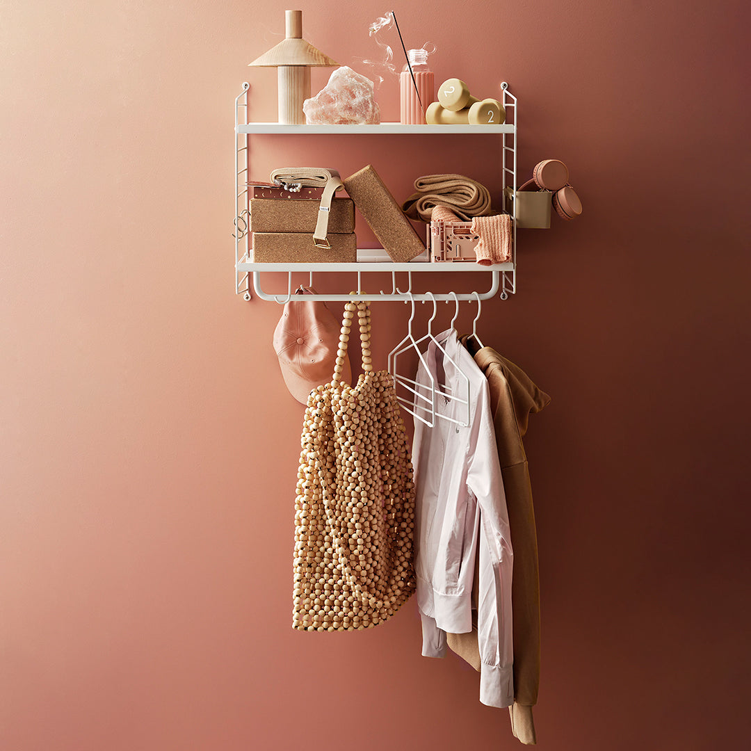 Stylish wall shelf displaying soft pink and neutral tones with a patterned golden bag and clothing items.