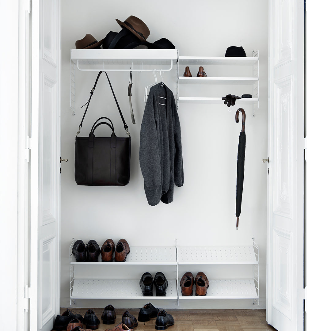 Minimalist white closet with black shoes, dark gray clothing, and various brown hats. Clean, modern design.
