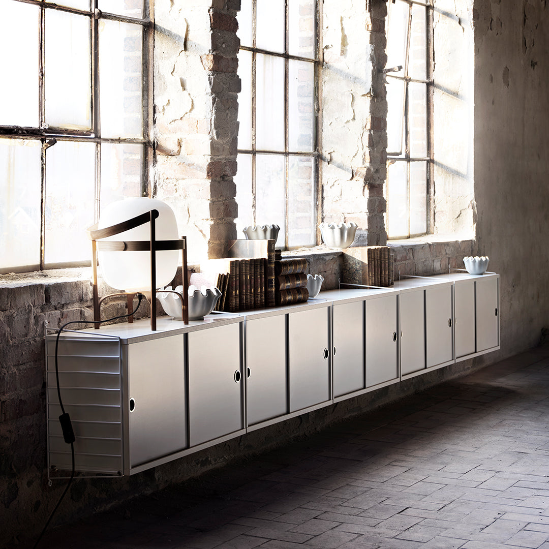 Sleek white storage cabinet with minimalist design, showcasing clean lines against rustic brick walls and natural light.