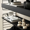 Black metal shelving with a minimalist pattern, featuring white notebooks and beige decorative items.