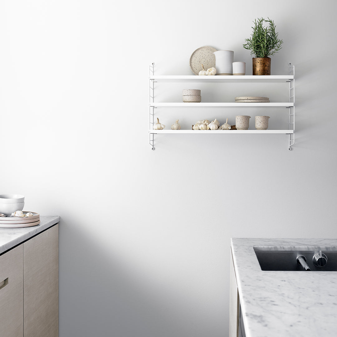 White shelving unit with neutral ceramics and greenery against a light gray wall and marble countertop. Clean, minimalist design.