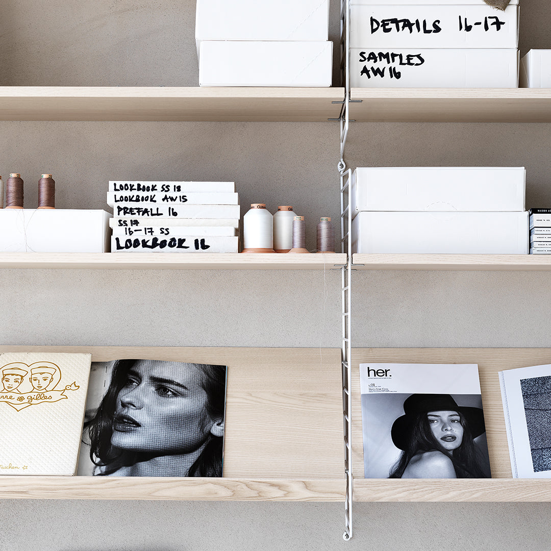 Minimalist shelves showcasing white boxes, light wood, and black and white magazine covers, creating a sleek, modern aesthetic.