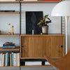 Wooden cabinet with a warm finish, paired with a textured plant pot and sleek black artwork on a modern shelf.