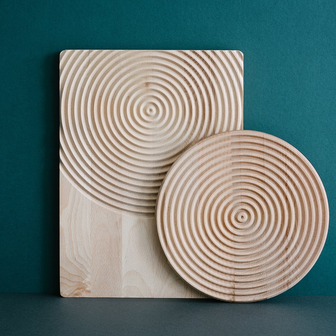 Natural wood serving set featuring a circular ripple pattern on a round plate and rectangular board, against a teal backdrop.