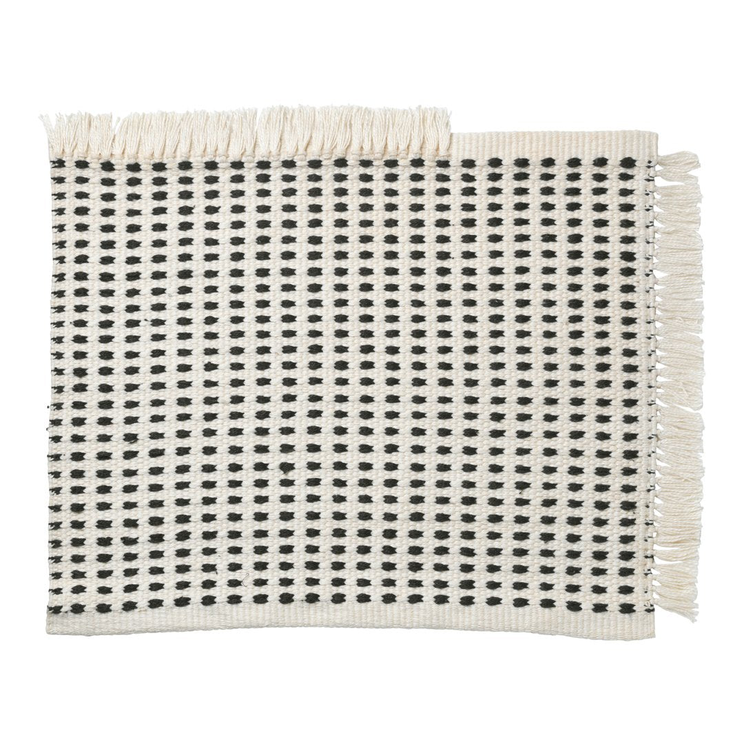 Woven cream placemat featuring a black square pattern with fringed edges for a chic, modern look.