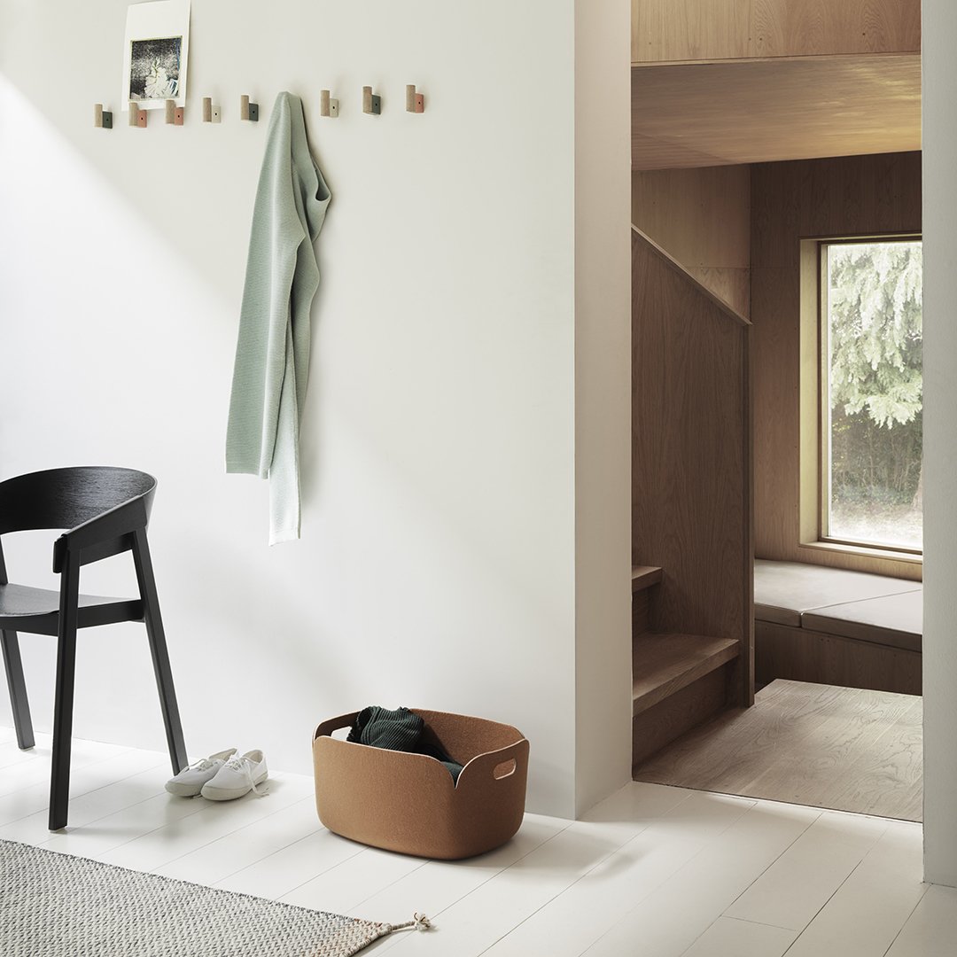Brown storage basket on light wood floor, complemented by green and neutral tones in a minimalistic interior setting.