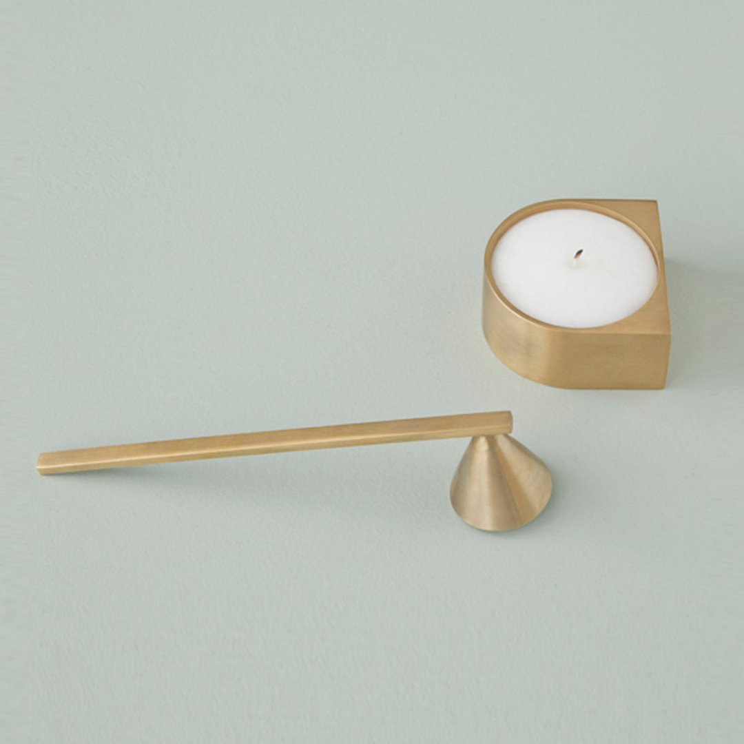 Gold candle holder and snuffer on a soft green background, showcasing sleek geometric shapes and smooth finishes.