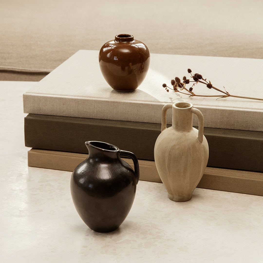 Three decorative vases in earthy tones of brown, beige, and black, featuring smooth finishes and elegant shapes.