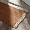 Brown woven rug with subtle texture and fringe in a warm, earthy tone. Perfect for cozy home decor.