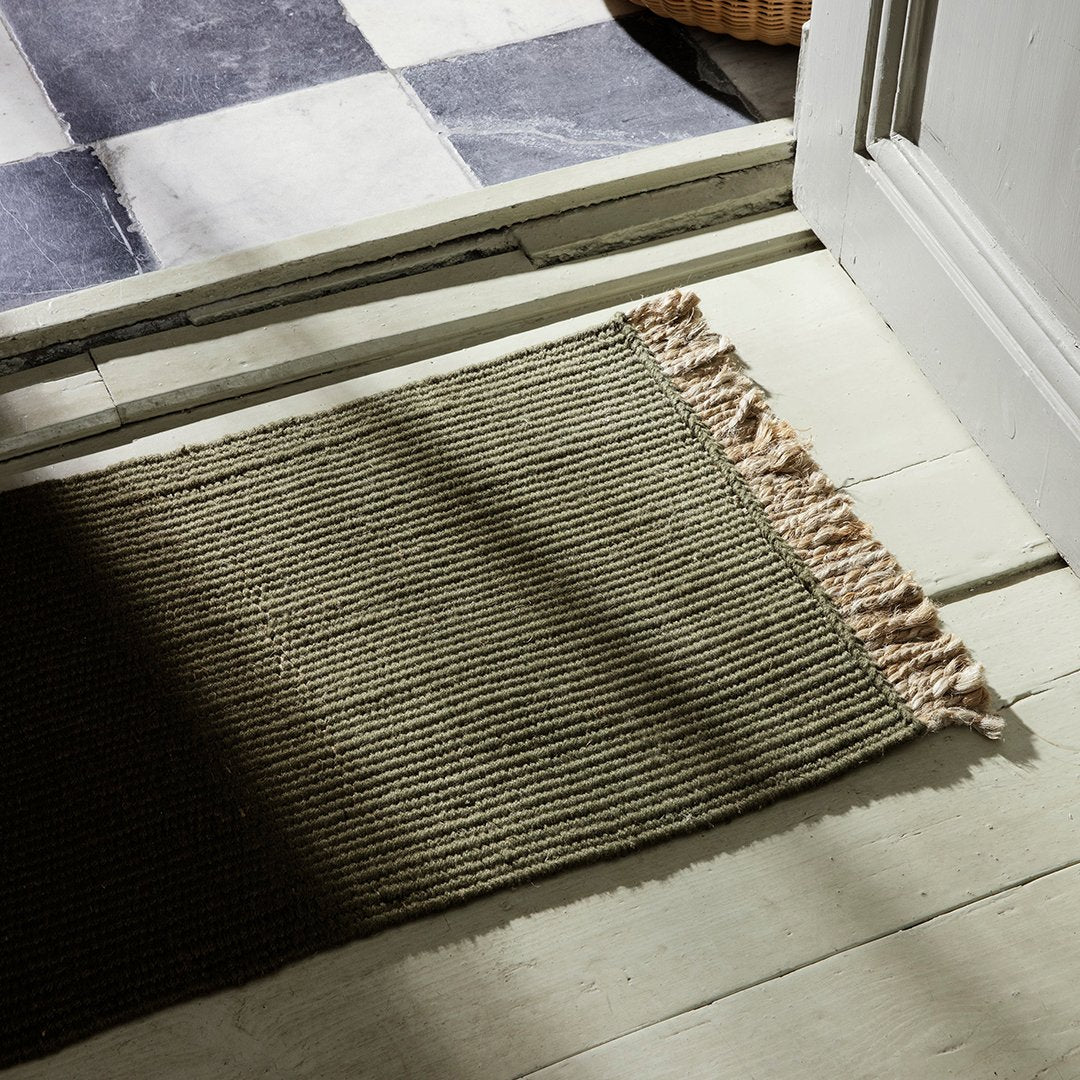 Olive green ribbed rug with beige fringes, complementing a checkered black-and-white floor.