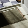 Olive green ribbed rug with beige fringes, complementing a checkered black-and-white floor.