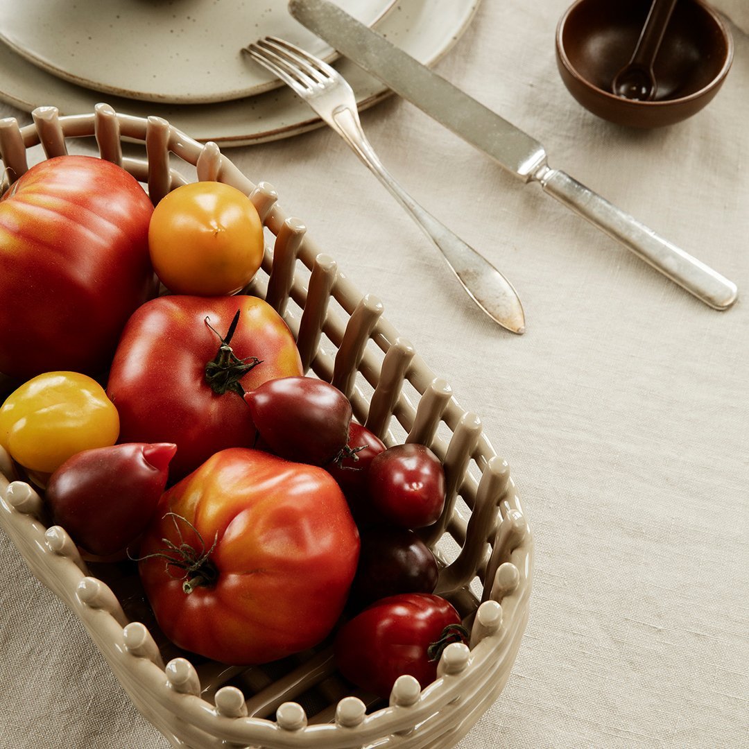 "Colorful assortment of red and yellow tomatoes in a woven basket on a textured neutral tablecloth."