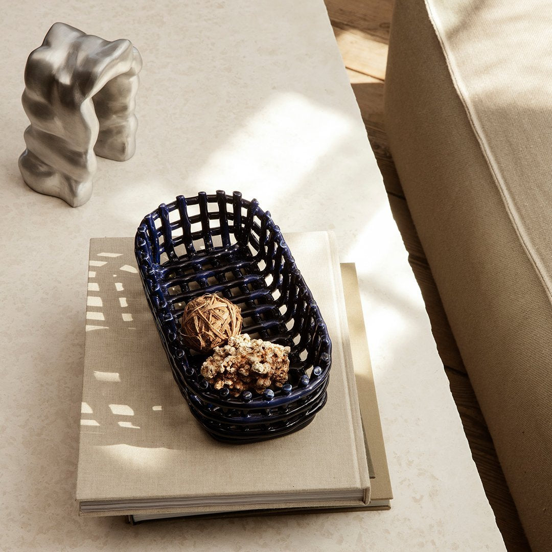 Navy blue woven basket with an open pattern, featuring natural decor accents, on a light beige tabletop.