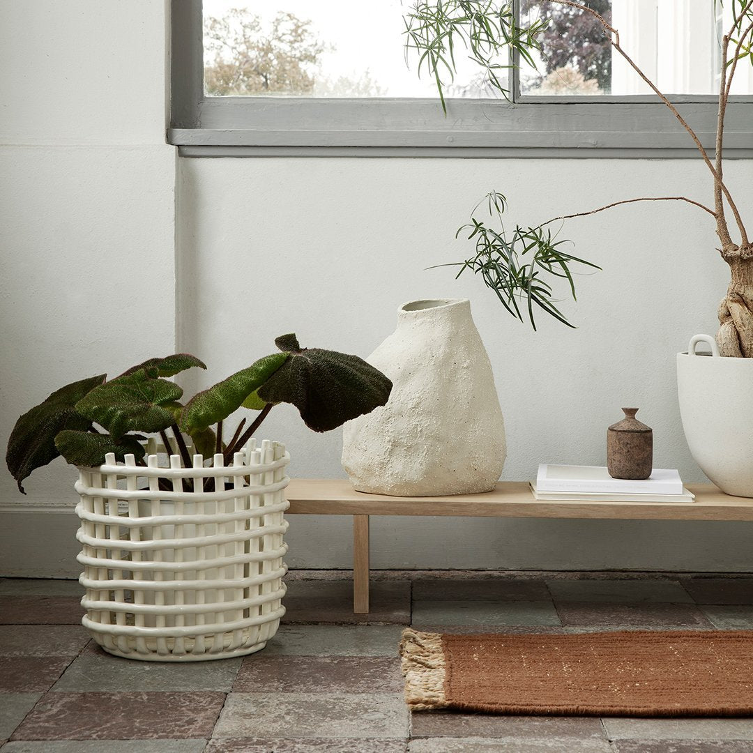 White woven plant basket with textured patterns, earthy tones of clay vase and rust-colored rug, creating a natural aesthetic.