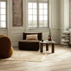 Cozy brown sofa with striped cushion, round mustard chair, and neutral textured rug in a bright, airy room.