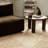 Brown plush couch with a cream geometric patterned rug and a minimalist round table in a warm, neutral-toned room.