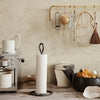 White paper towel holder on a wooden surface, surrounded by neutral tones and various kitchen utensils in muted colors.