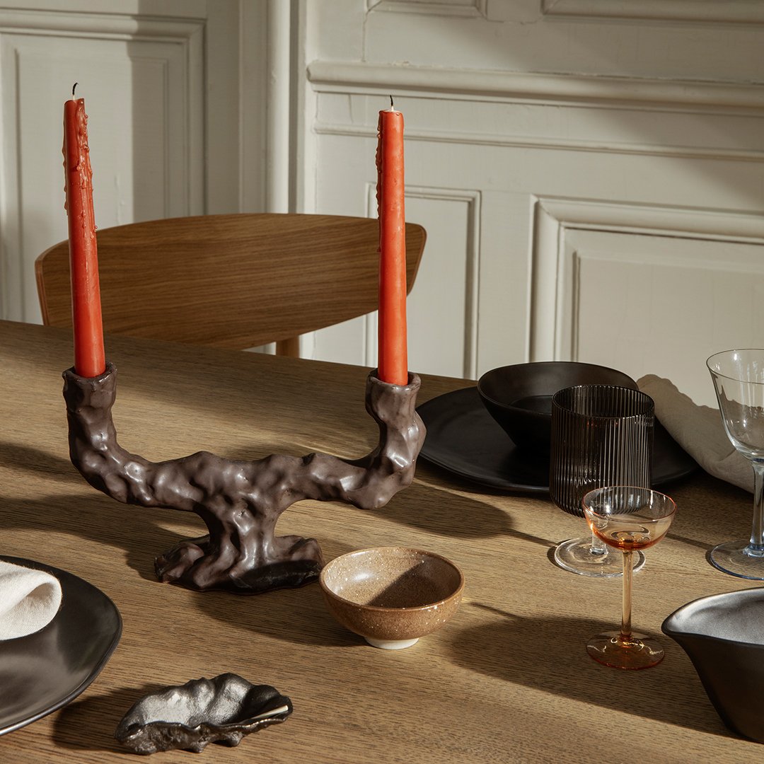 "Unique brown candlestick holder with red candles on a wooden table, complemented by various dishware and glassware."