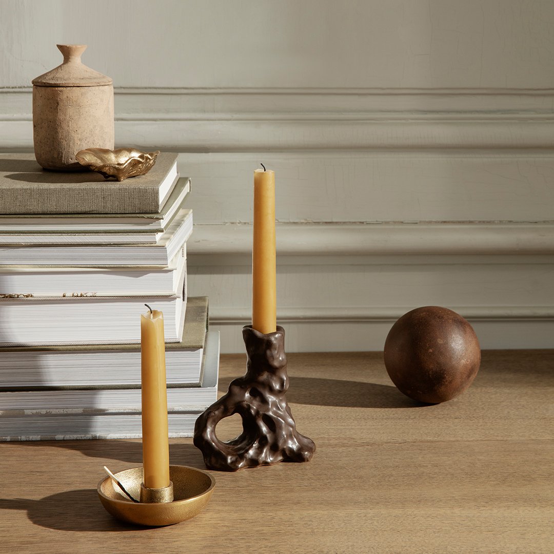 "Warm amber candles with a textured brown holder, atop neutral-colored books and a smooth brown decorative orb."