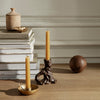 "Warm amber candles with a textured brown holder, atop neutral-colored books and a smooth brown decorative orb."