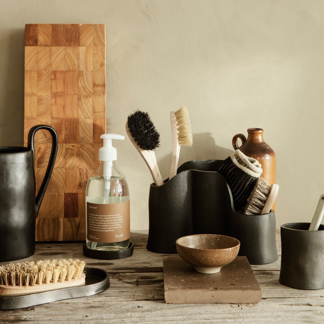 Black ceramic utensils and brushes on a wooden table, complemented by a beige wall and natural textures.