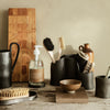 Black ceramic utensils and brushes on a wooden table, complemented by a beige wall and natural textures.