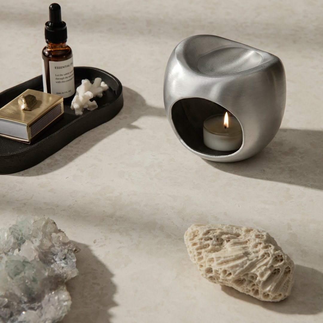 Silver candle holder on a light beige surface, accompanied by dark tray and various natural stones.