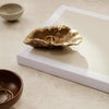 Gold organic-shaped dish on a white surface, surrounded by earthy brown and muted gray ceramic items.