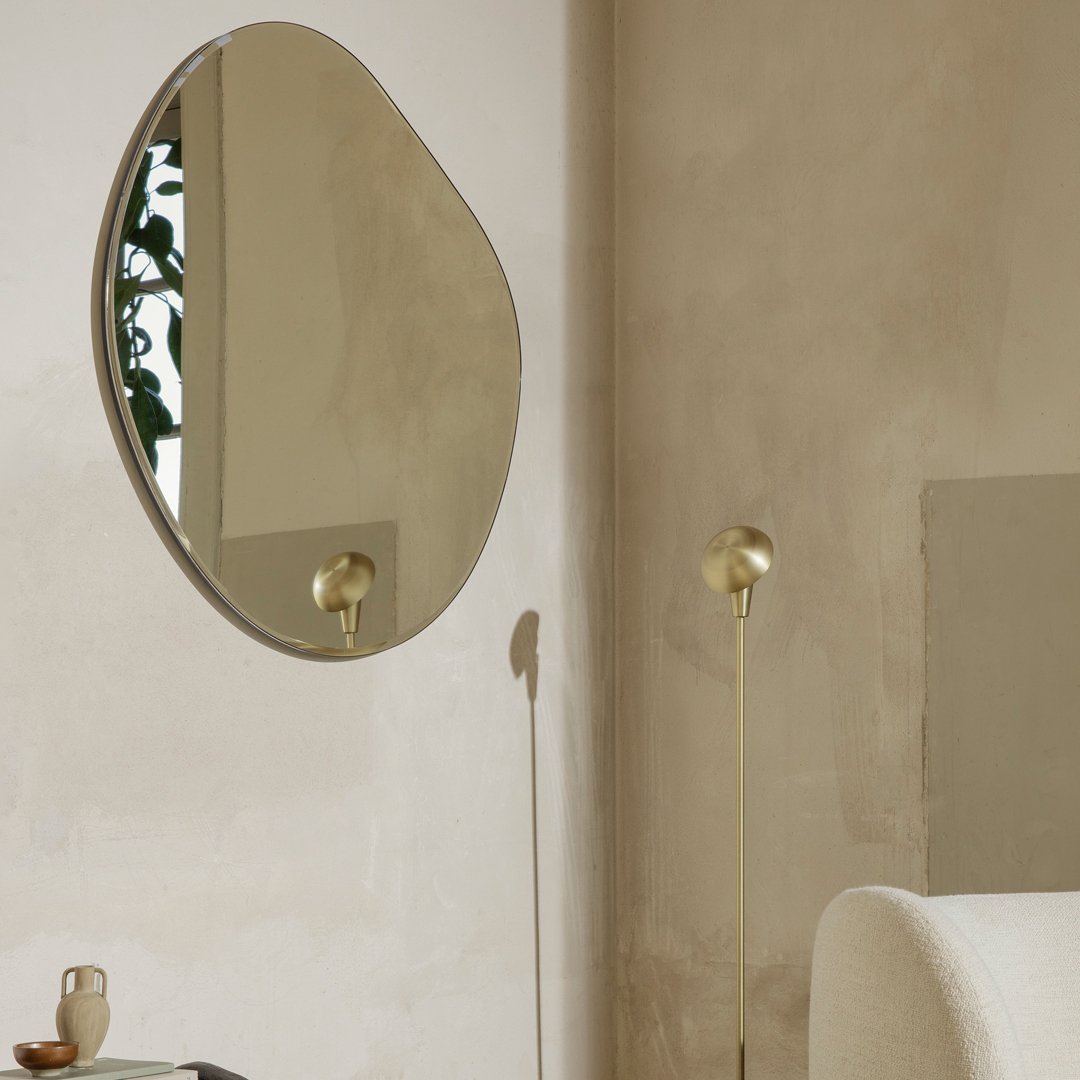 Reflective, organic-shaped wall mirror with polished silver edges, set against a warm, neutral-toned wall.