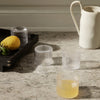 Clear ribbed glass cups in translucent and frosted finishes, set on a marble surface with lemon accents.