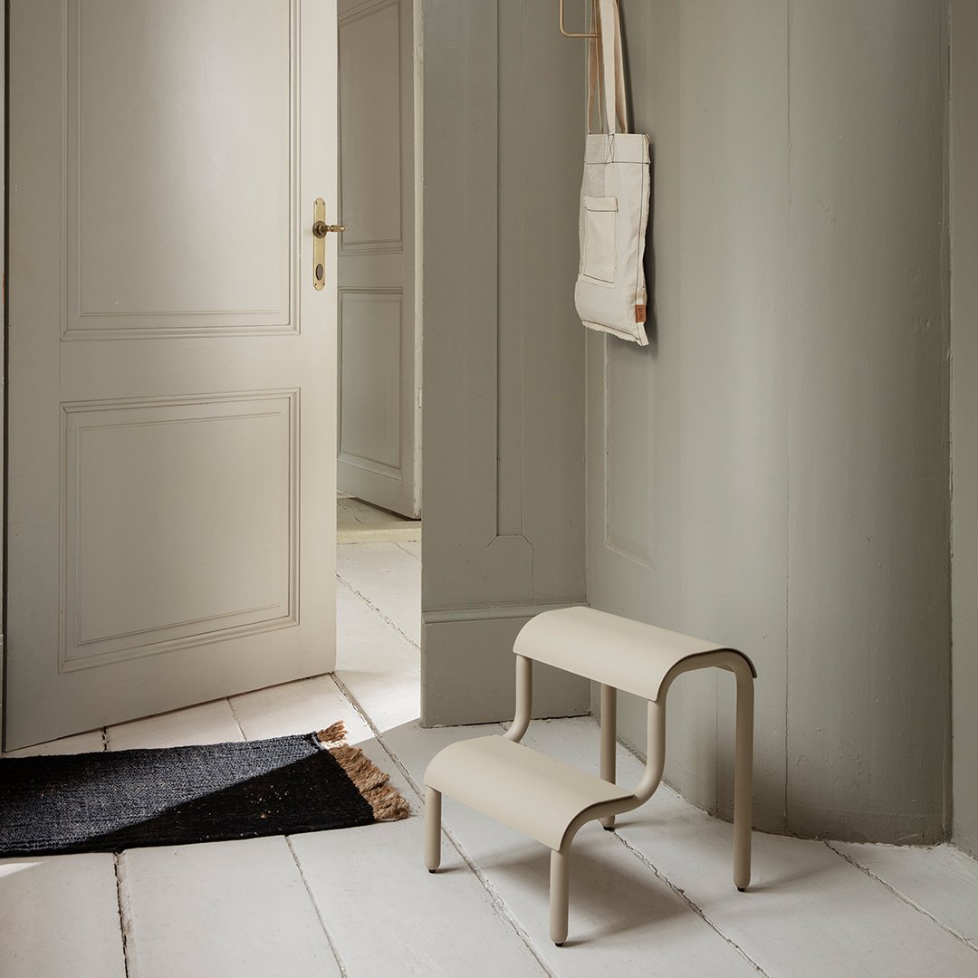Beige two-step stool against a soft gray wall, with a subtle textured pattern on the floor mat.