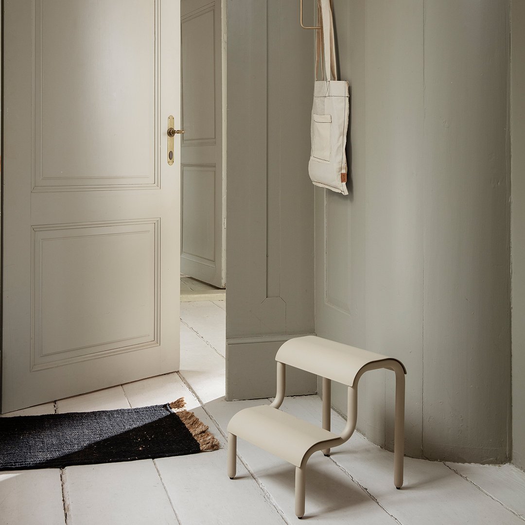 Beige two-step stool with smooth curves, set against a subtle gray wall and white flooring, creating a minimalist aesthetic.