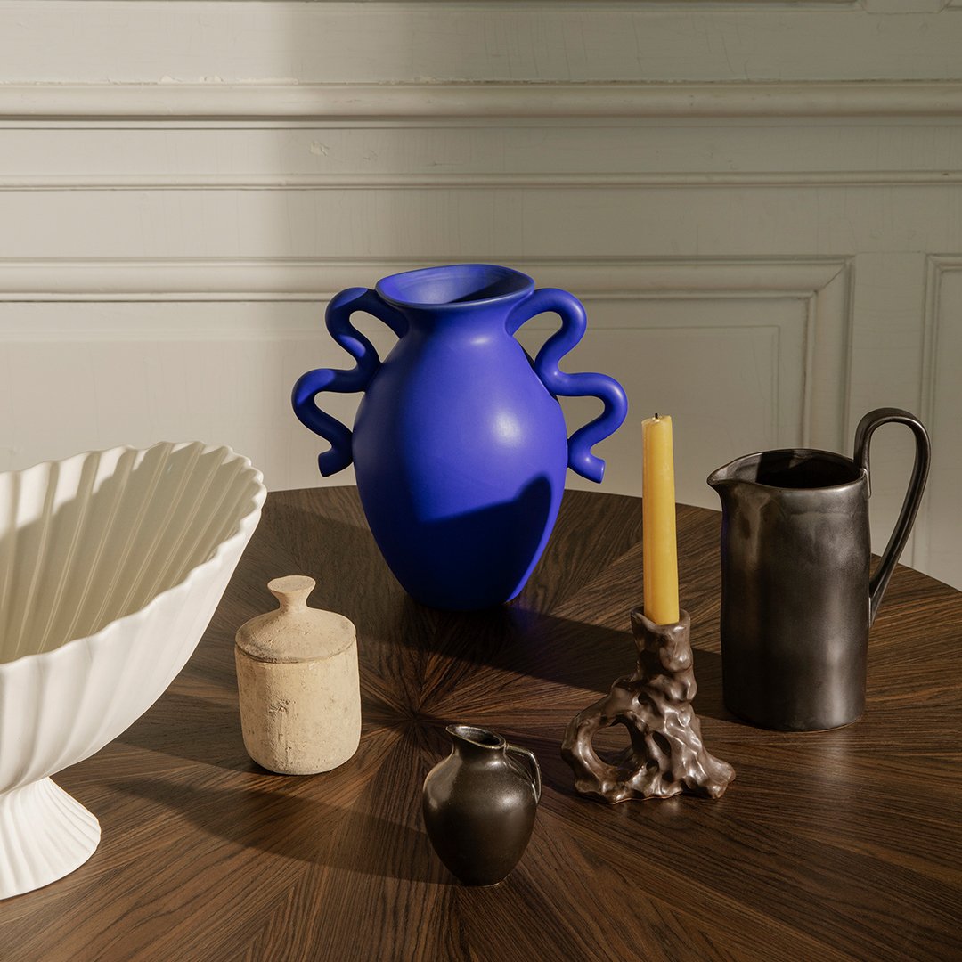 "Vibrant blue vase with unique handles, white textured bowl, and black matte pitcher on a wooden table."