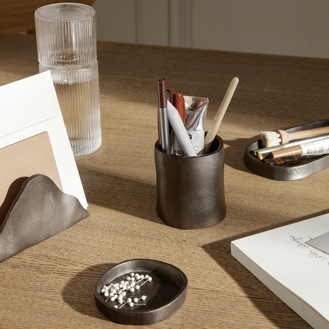 Matte black desk organizer with subtle curves and a sleek finish, complemented by a textured gray dish and a light wooden surface.