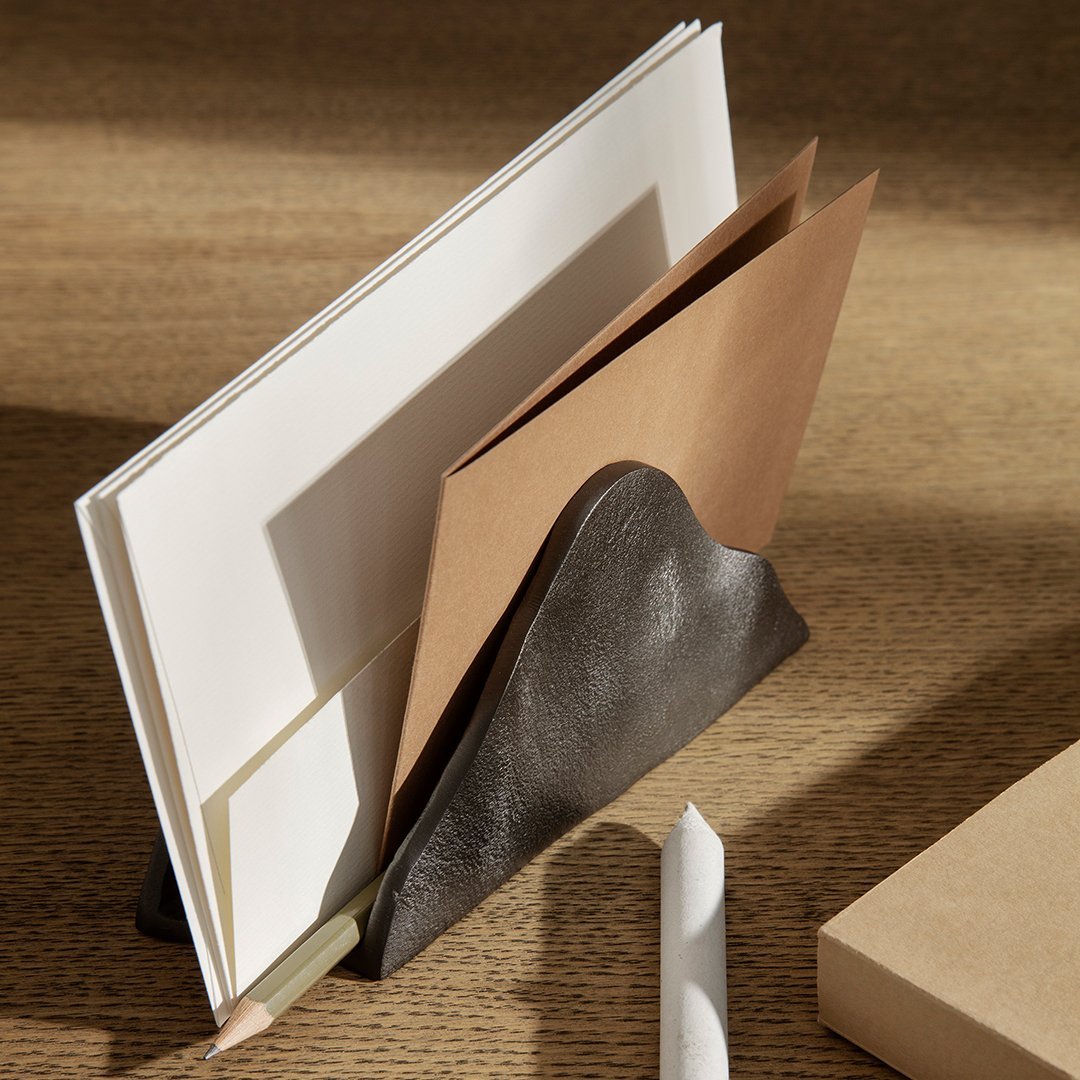Brown and white paper stacked in a stylish dark gray leather holder on a wooden surface. Minimalist design.