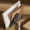 Brown and white paper stacked in a stylish dark gray leather holder on a wooden surface. Minimalist design.