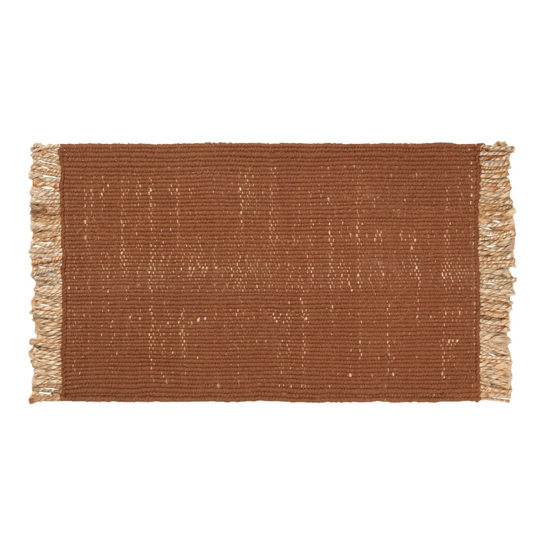 Rust-colored woven rug with fringe edges, featuring a textured, subtle pattern. Perfect for warm home decor.