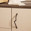 "Beige cabinet with a wavy black handle and a textured cream towel on a dark countertop."