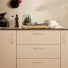"Neutral beige cabinet with wavy gold handles, complemented by elegant glassware and a minimalist table setting."