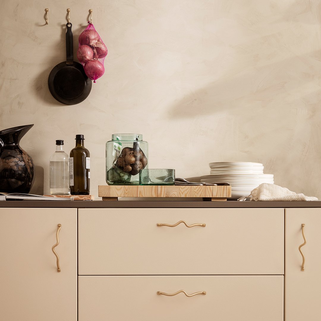 Elegant beige cabinet with gold hardware, layered textures, and vibrant accents of green, black, and purple in kitchen decor.