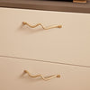 Gold wave-patterned drawer handles on a smooth cream and gray dresser, adding a modern touch to furniture design.