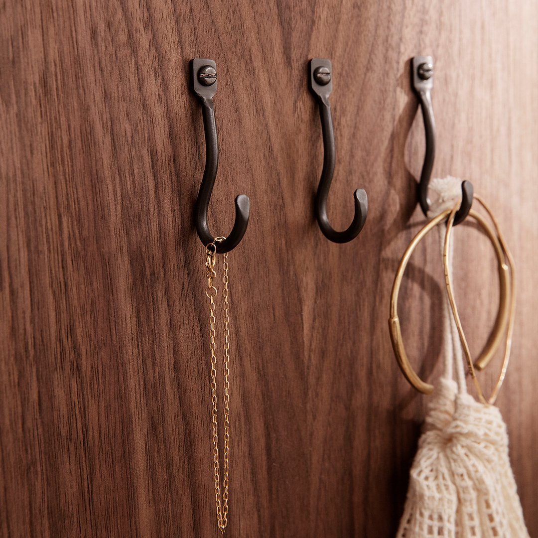 "Three black iron hooks on a rich brown wooden background, displaying gold and textured white accessories."