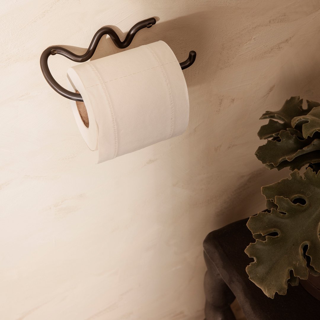 White toilet paper roll on a modern black holder against a soft beige wall, complemented by green foliage.