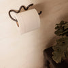 White toilet paper roll on a modern black holder against a soft beige wall, complemented by green foliage.
