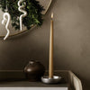 Tall amber candle in silver holder, dark ceramic vase, white decor accents, and rich earthy tones.