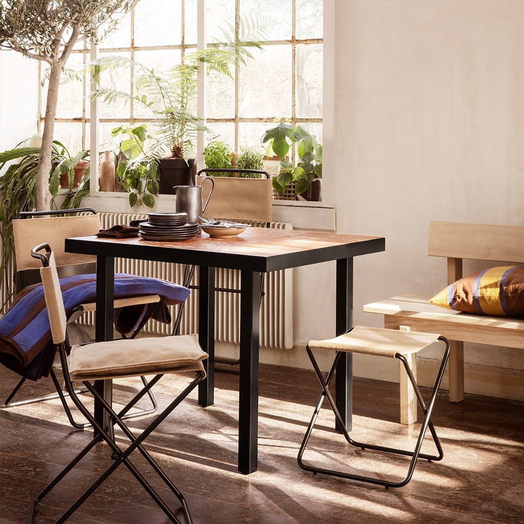 "Square wooden table with a dark frame, surrounded by light-colored chairs and vibrant striped cushions."